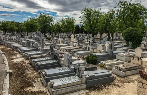 Fotografía de cuidadores de patio trabajando en un cementerio, con herramientas de jardinería y rodeados de tumbas adornadas.