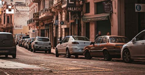 Foto de una calle con coches aparcados en un centro urbano, con siluetas de personas