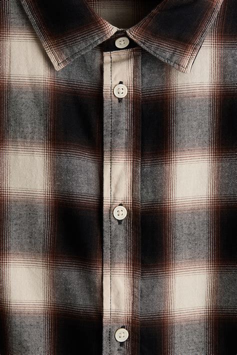 Fotografía de estudio de una camisa de franela a cuadros en tonos café, mostrando la textura del tejido y los detalles del cuello.