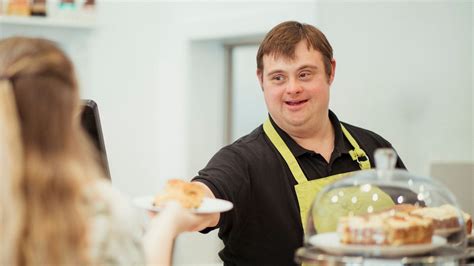 Foto de jóvenes con síndrome de Down trabajando en un restaurante o tienda, sonriendo e interactuando con clientes o compañeros.