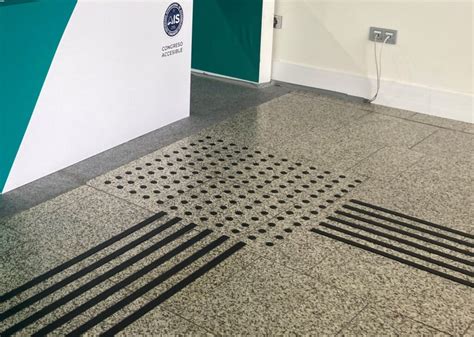 Persona con bastón guiándose por pavimento podotáctil en un entorno urbano