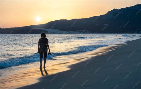 Mujer mayor caminando por la orilla del mar al atardecer