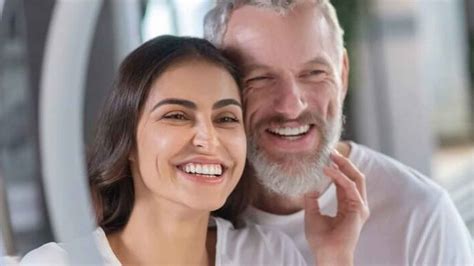 Foto de una pareja con gran diferencia de edad caminando de la mano en un espacio público, con miradas curiosas de fondo