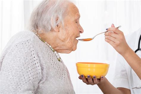 Ilustración de una persona alimentando a un paciente con disfagia en una postura adecuada con cuchara pequeña