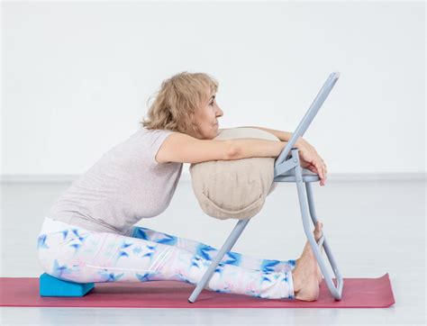 Imagen de una persona mayor practicando yoga en silla con una sonrisa, con un monitor asistiéndole