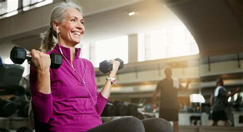 Mujer mayor realizando ejercicios de fuerza en un gimnasio, sonriendo.