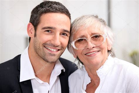 Madre anciana y su hijo adulto caminando de la mano en un parque, con árboles y luz suave