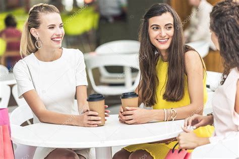 Mesa de cafetería con mujeres jóvenes sentadas, mientras mujeres mayores observan