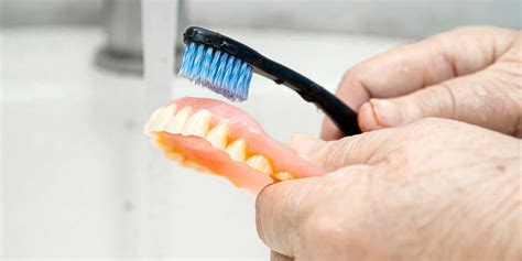 Foto de una persona mayor cepillándose los dientes o limpiando una prótesis dental