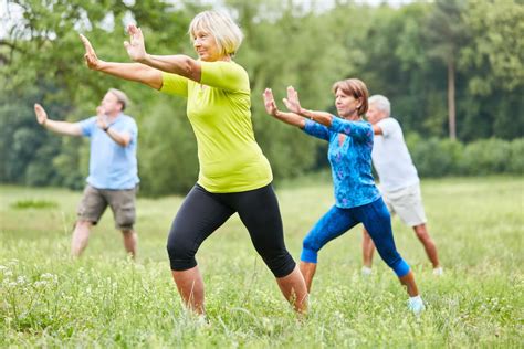 Un grupo de adultos mayores practicando ejercicios suaves al aire libre, posiblemente Tai Chi o yoga.