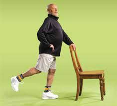 Persona mayor realizando ejercicio de equilibrio con apoyo en una silla