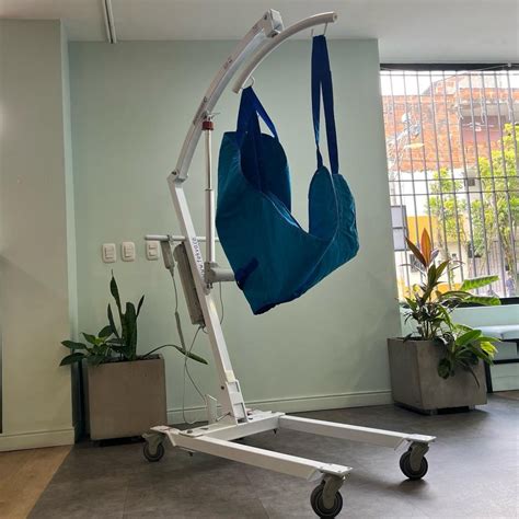 Foto de una grúa eléctrica de traslado de pacientes en uso, con un cuidador asistiendo a una persona