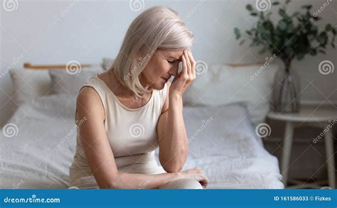 Mujer mayor sentada en la cama, mirando con preocupación el reloj