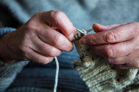 Manos de una persona mayor tejiendo una bufanda.