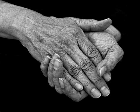Pareja de adultos mayores tomándose de las manos en blanco y negro, con enfoque en las arrugas y la textura de la piel