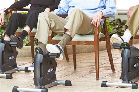 Persona mayor utilizando una pedalera estática sentada en una silla