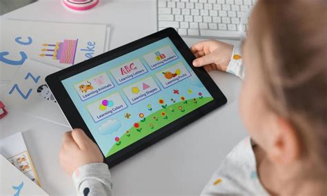 Un niño utilizando una aplicación interactiva en una tableta para aprender letras y palabras, con pictogramas visibles en la pantalla.