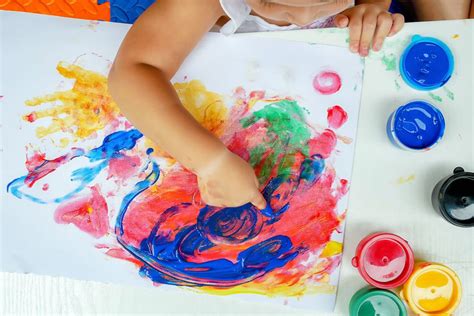 Niño con las manos cubiertas de pintura de dedos explorando una superficie de papel con diferentes texturas.