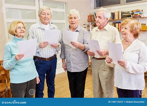 Grupo de adultos mayores cantando en un taller, con partituras y un ambiente alegre