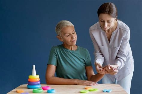 Terapeuta ocupacional interactuando con un cuidador y la persona dependiente, adaptando el entorno o enseñando técnicas.