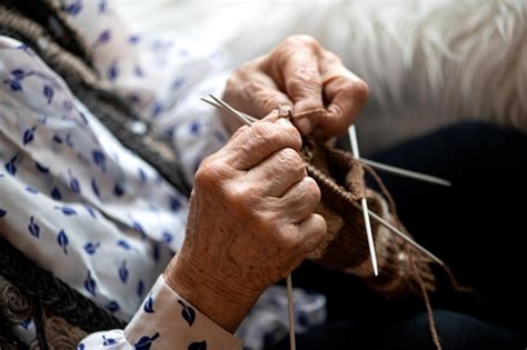 Manos de anciana tejiendo o cosiendo, con una aguja e hilo