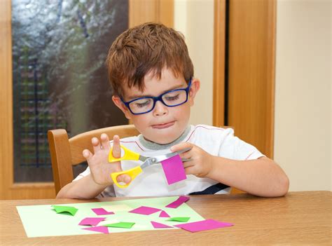 Niño feliz usando tijeras adaptadas para cortar papel en el aula
