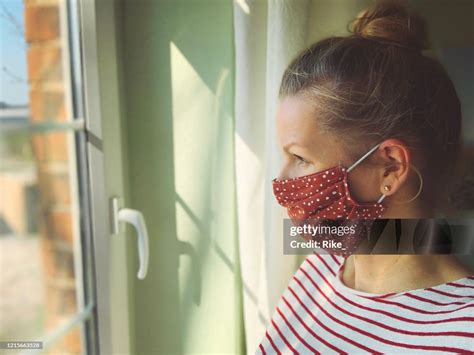 Pretty woman in quarantine with mask, looks out the window