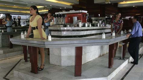 Vista interior de un café con piernas tipo Haití, con una barra alta y espejos, mostrando a una mesera en vestido corto
